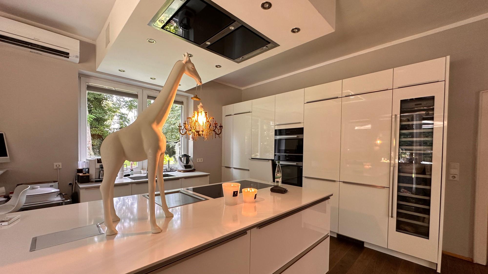 In einer geräumigen weißen Küche steht eine weiße Lampe in Form einer Giraffe auf dem Tresen, der auch das Spülbecken enthält.
