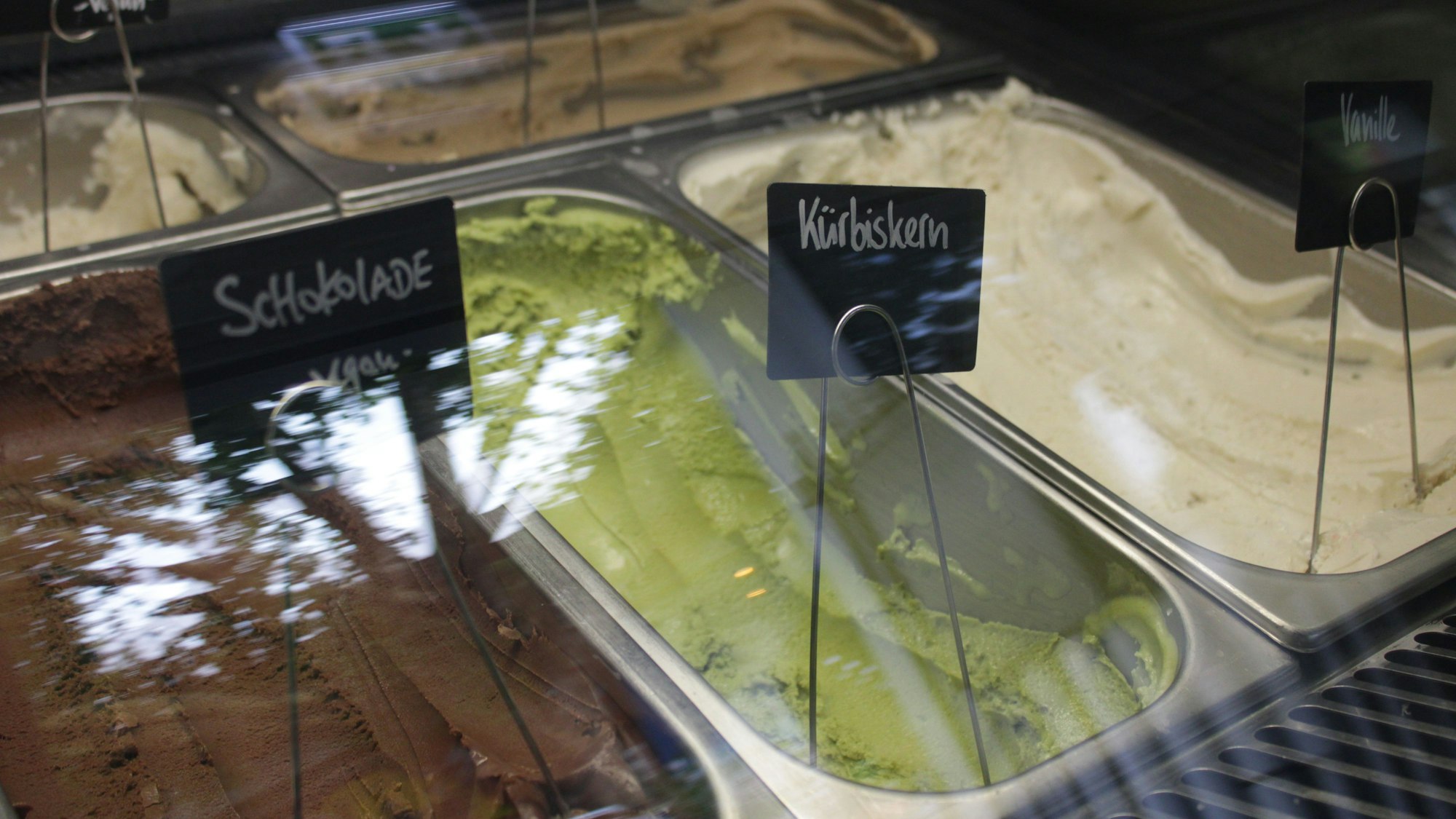 Veganes Schokoladeneis, grünes Kürbiskerneis und Vanilleeis in der Auslage einer Eisdiele.