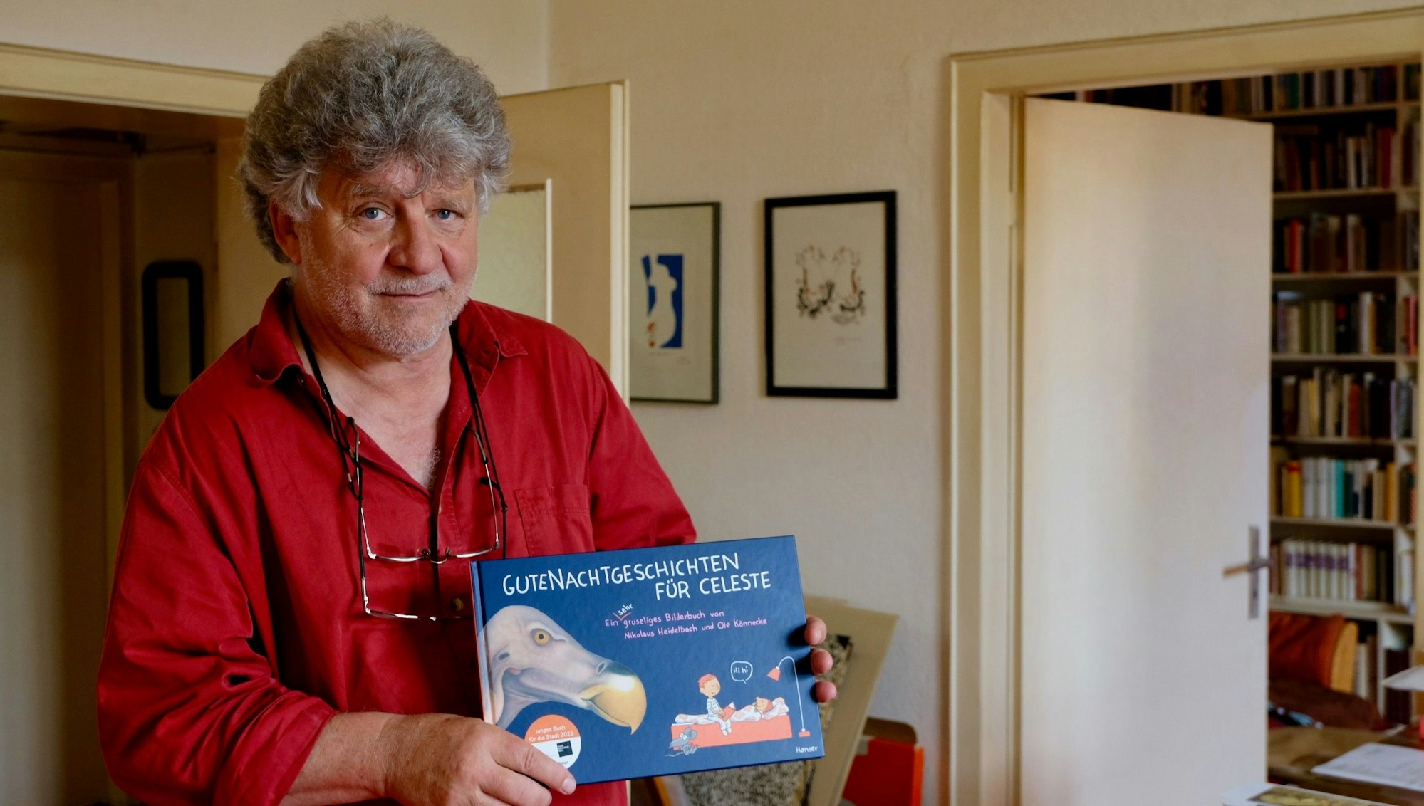 Ein Mann mit grauem Haar und rotem Hemd hält ein Buch in der Hand.