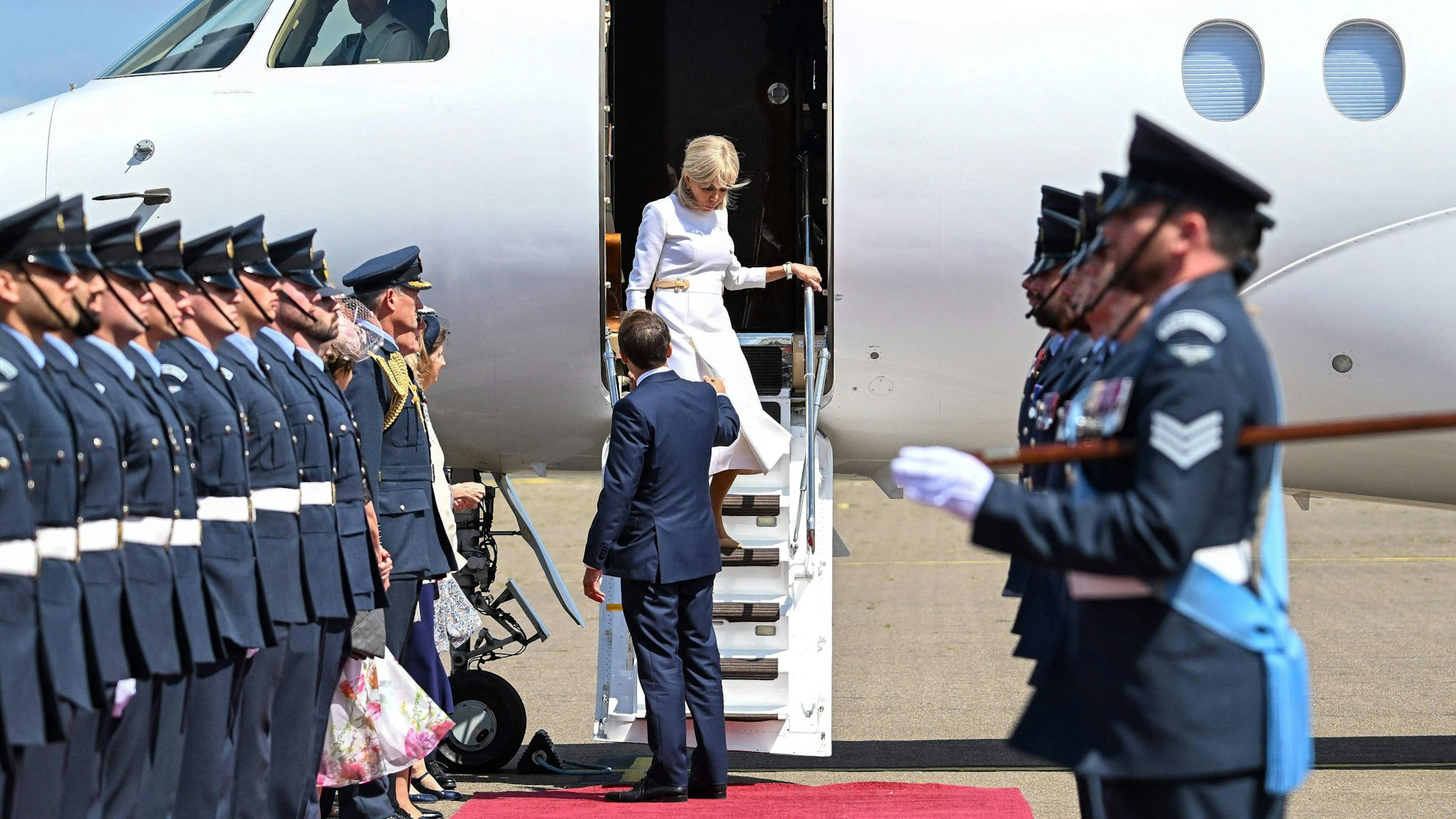 Brigitte Macron steigt aus dem Flugzeug aus. Ihr Mann steht vor ihr und reicht ihr die Hand.