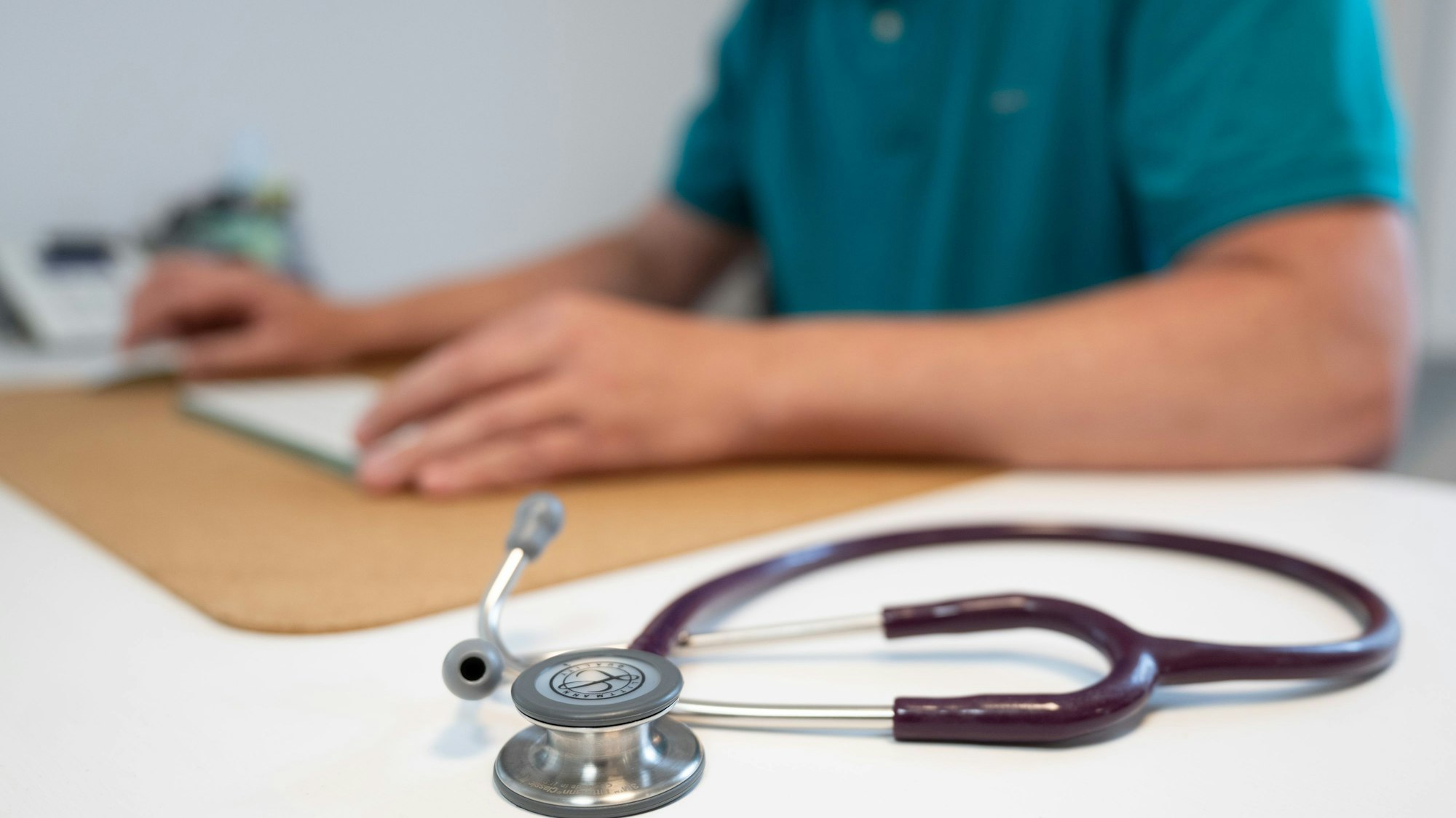 Ein Hausarzt sitzt in einem Sprechzimmer seiner Hausarztpraxis an einem Schreibtisch neben einem Stethoskop und arbeitet am Computer. (Symbolbild)