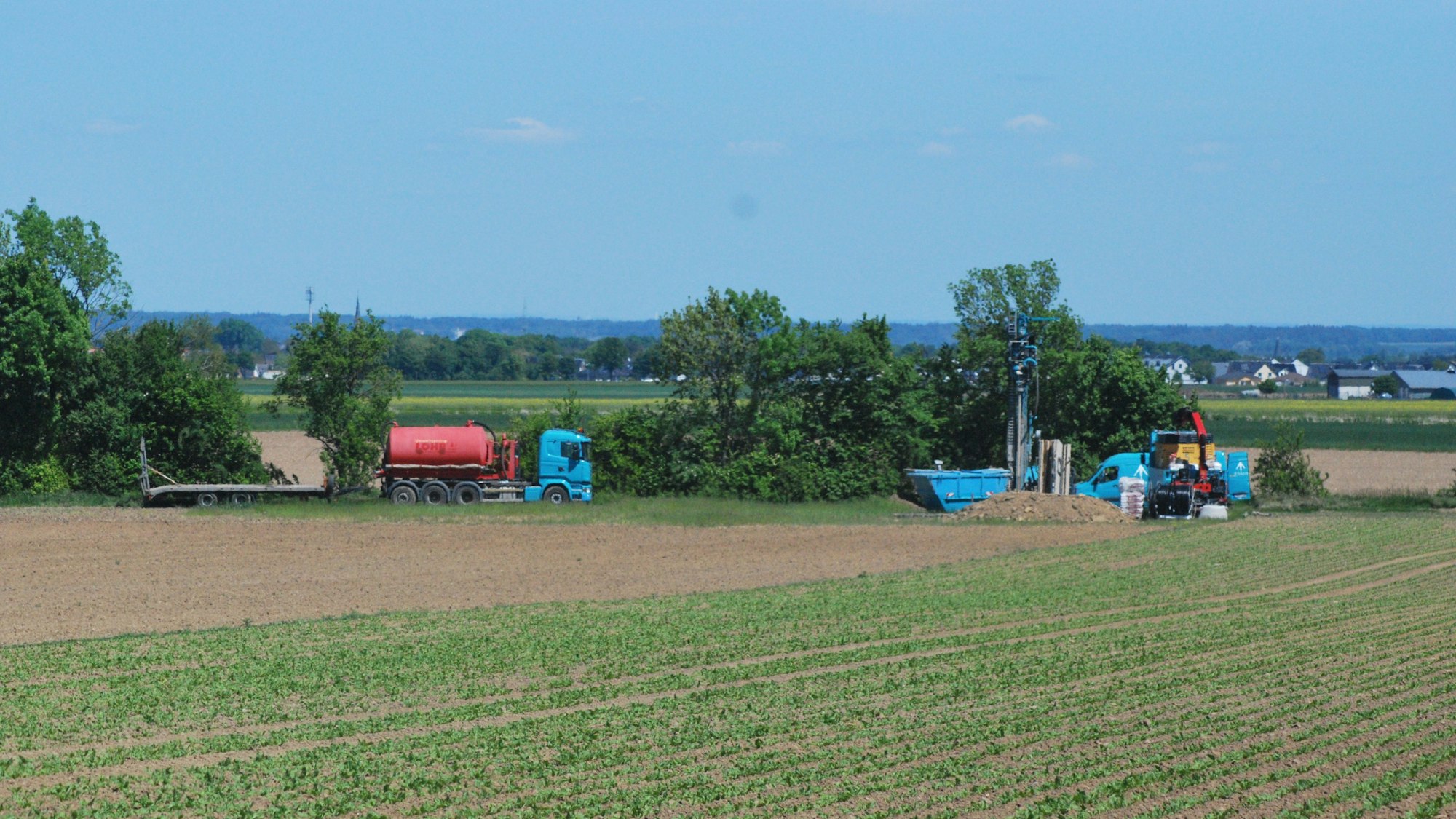 Das Bild zeigt ein Erdbohrgerät und einen Lastwagen am Rand eines Ackers.
