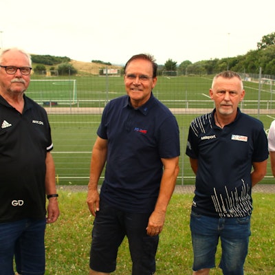 Vier Männer stehen vor einem Fußballplatz.