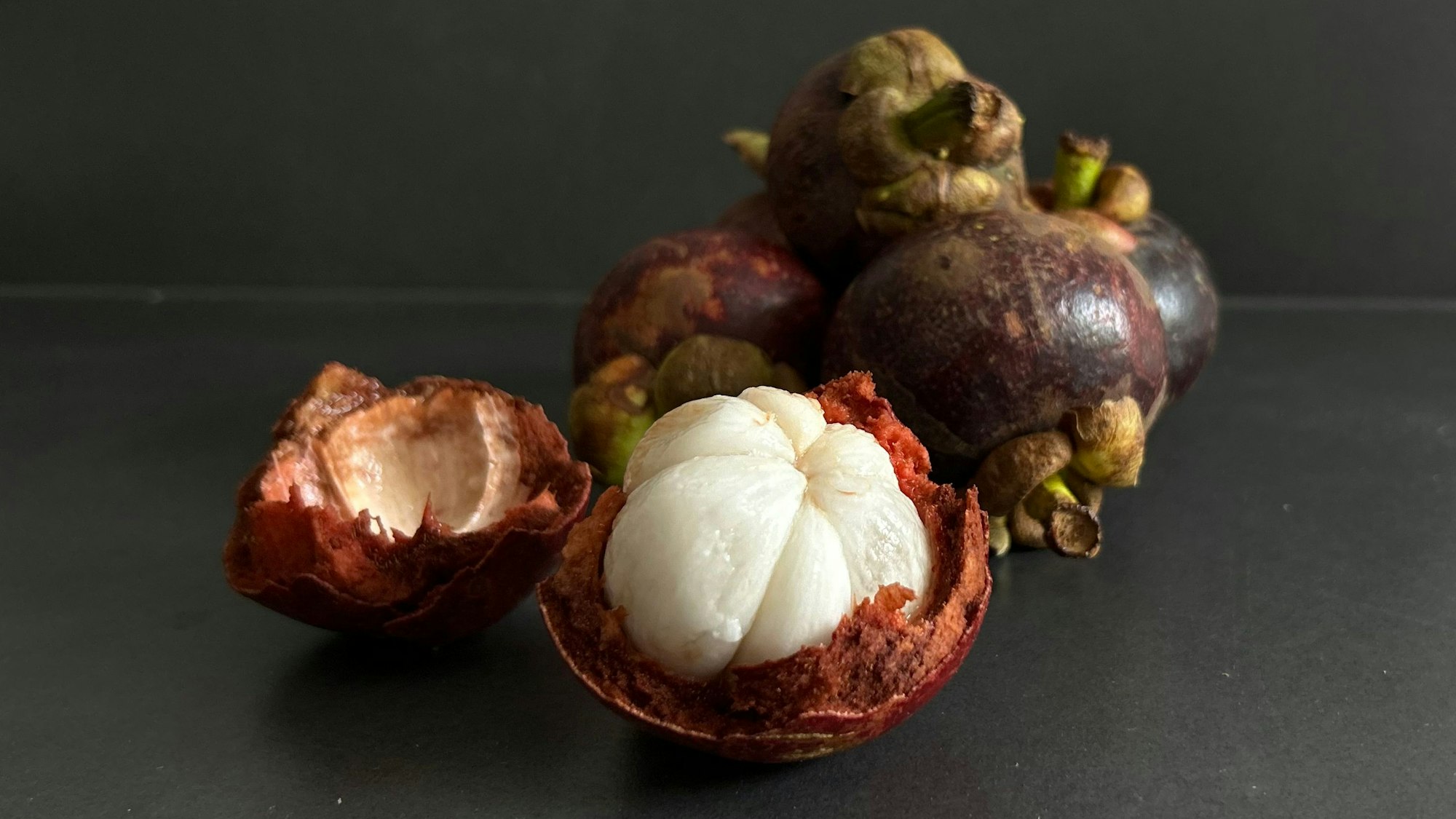 Von außen dunkelviolett und dickschalig, überrascht sie innen mit zartem, weißen Fruchtfleisch, das in Segmente geteilt ist, erinnert an Knoblauchzehen.