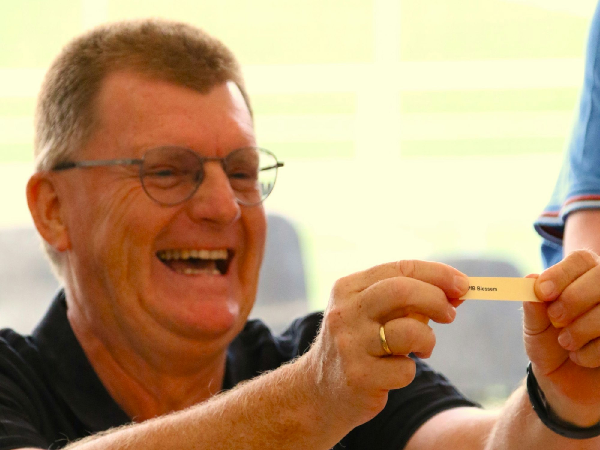 Peter Dierichsweiler hält einen Zettel vor sich und freut sich. Unterhalb seiner Brillengläser sind Lachfalten in seinem Gesicht.