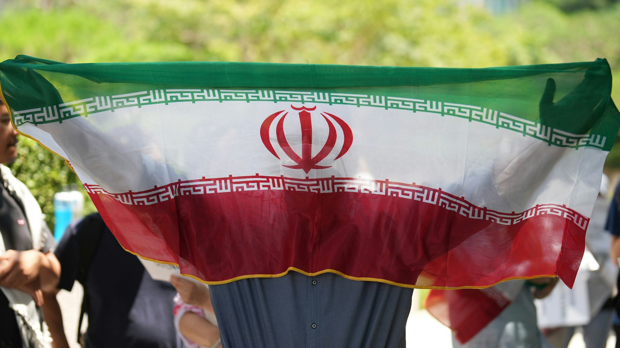 Ein Mann hält eine iranische Flagge während einer Kundgebung mit der Forderung, den Krieg zwischen Israel und dem Iran zu beenden