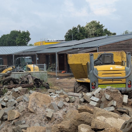 Das Foto zeigt Baufahrzeuge und Bauschutt vor dem Holzgebäude der Kita in Kalscheuren.