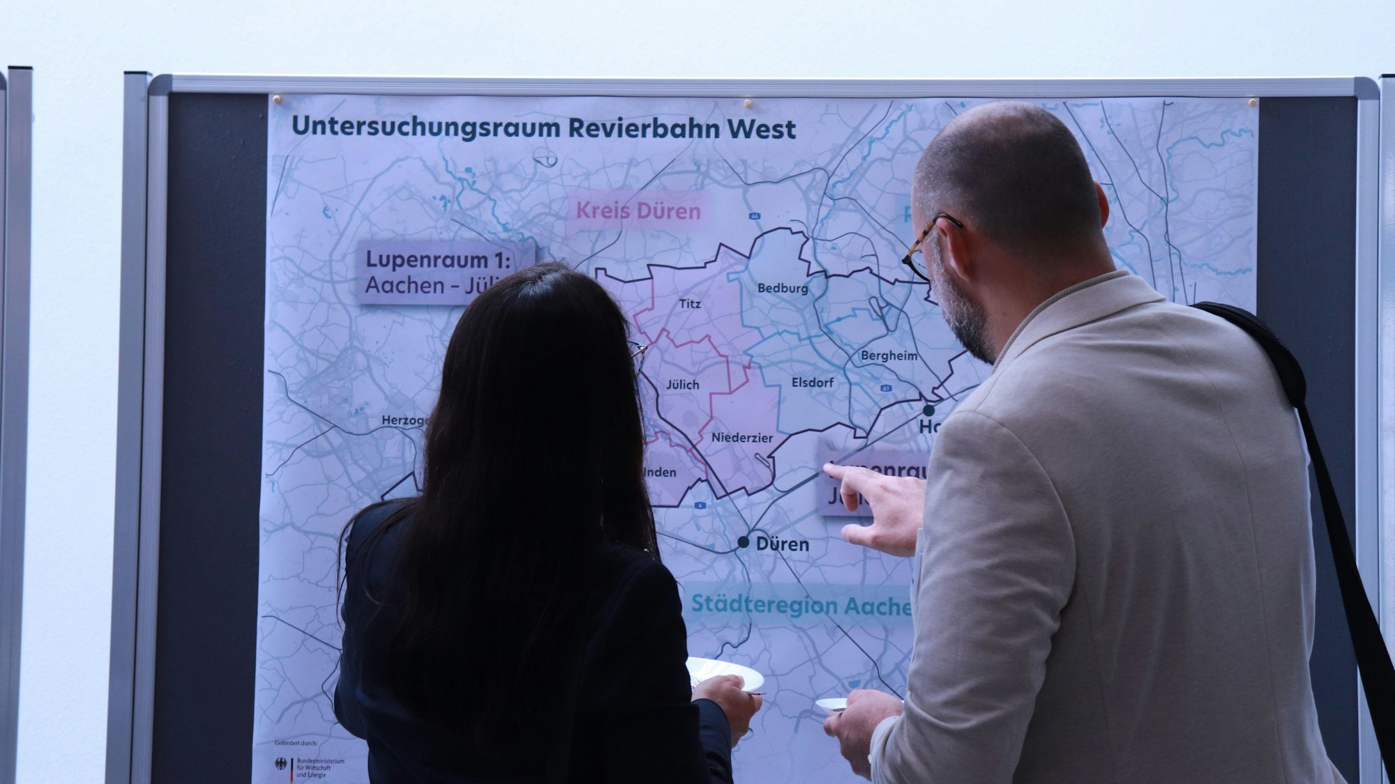 Eine Frau und ein Mann stehen vor einer Karte des Rheinischen Reviers.