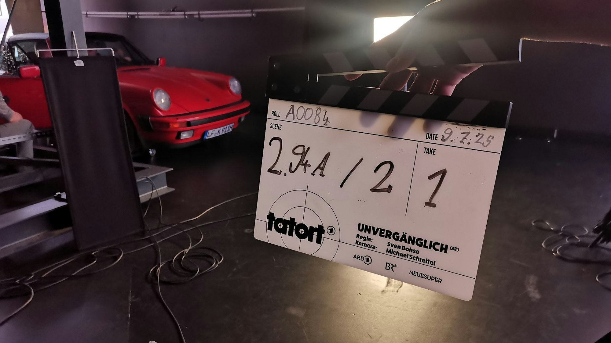 Ein roter Porsche neben einer Klapp, auf der der Filmtitel „unvergänglich“ steht.