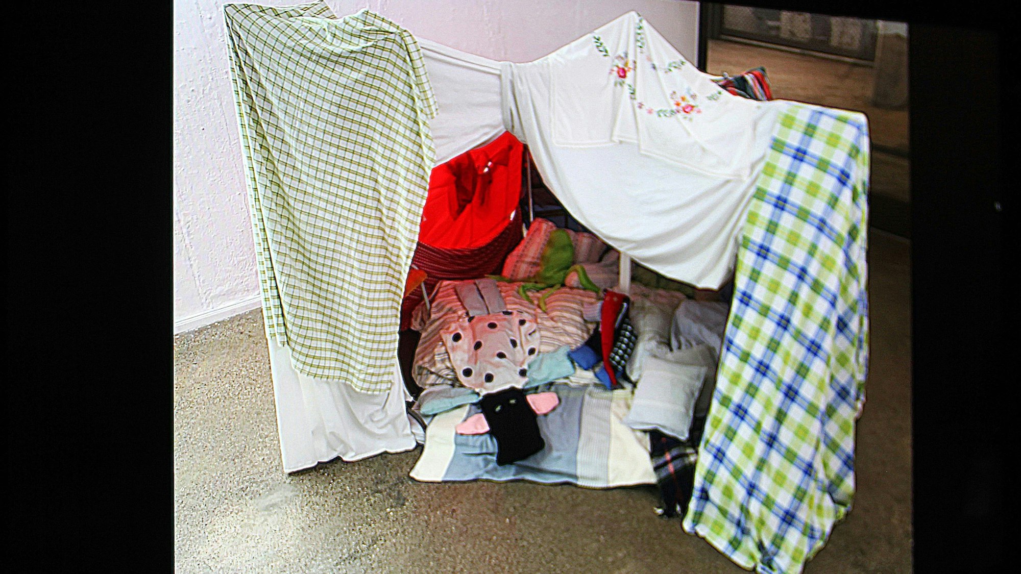 Zu sehen ist eine gebaute, textile Höhle aus bunten Laken und Kissen, aus der Ausstellung „soft intentions“.