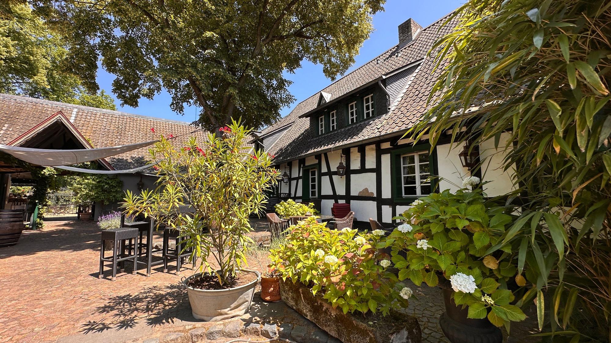 Ein Fachwerkhof mit Innenhof und blühenden Pflanzen ist zu sehen.