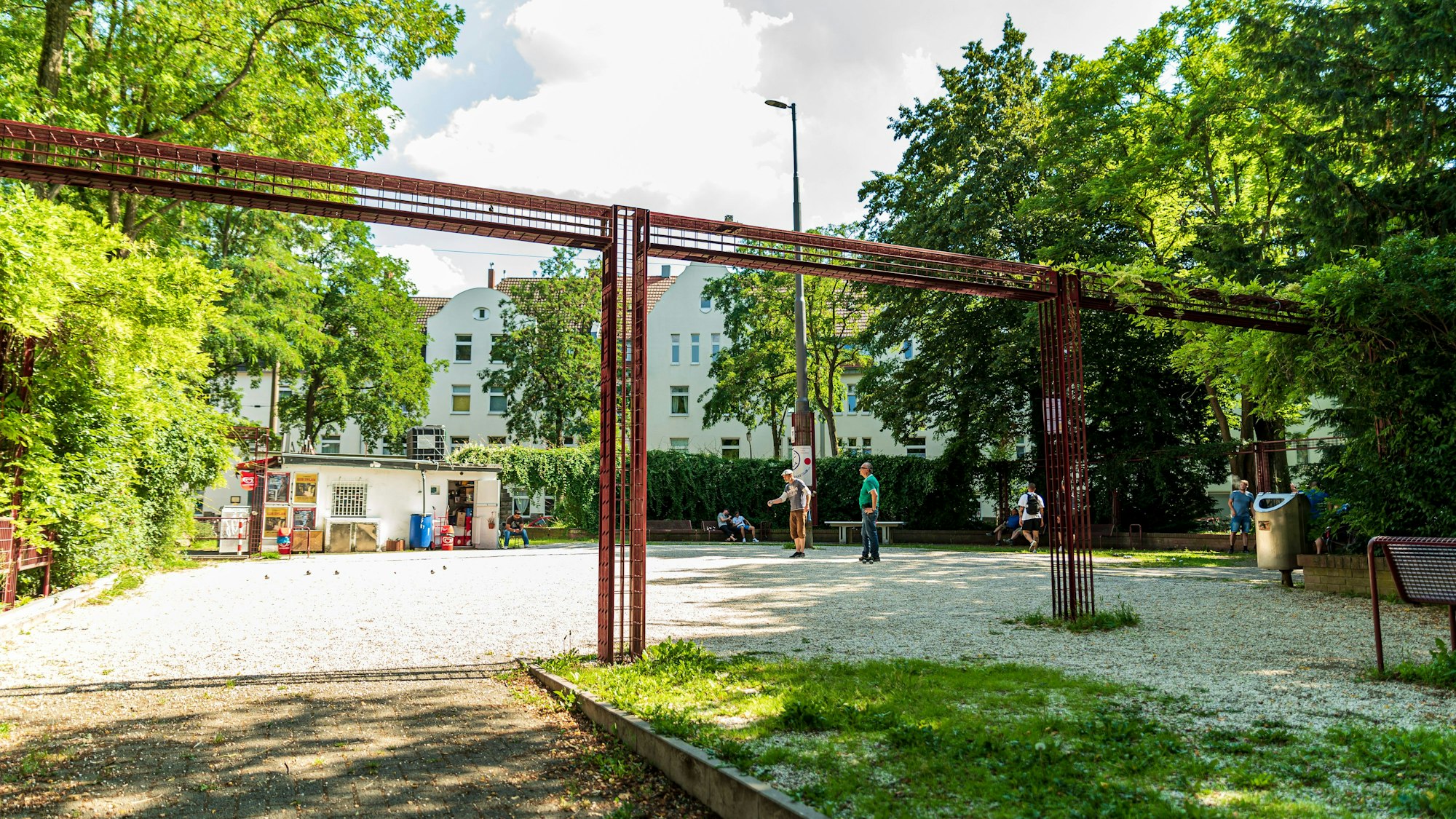 Ein Schotterplatz ist zu sehen, Leute spielen darauf Boule.