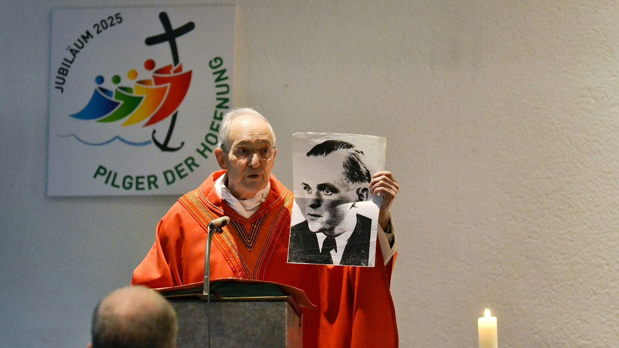 Prälat Helmut Moll hält ein Schwarz-weiß-Foto eines Mannes hinter der Kanzel in die Luft.