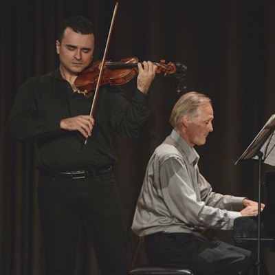 Zwei Musiker auf der Bühne – einer am Klavier und der andere mit Geige.