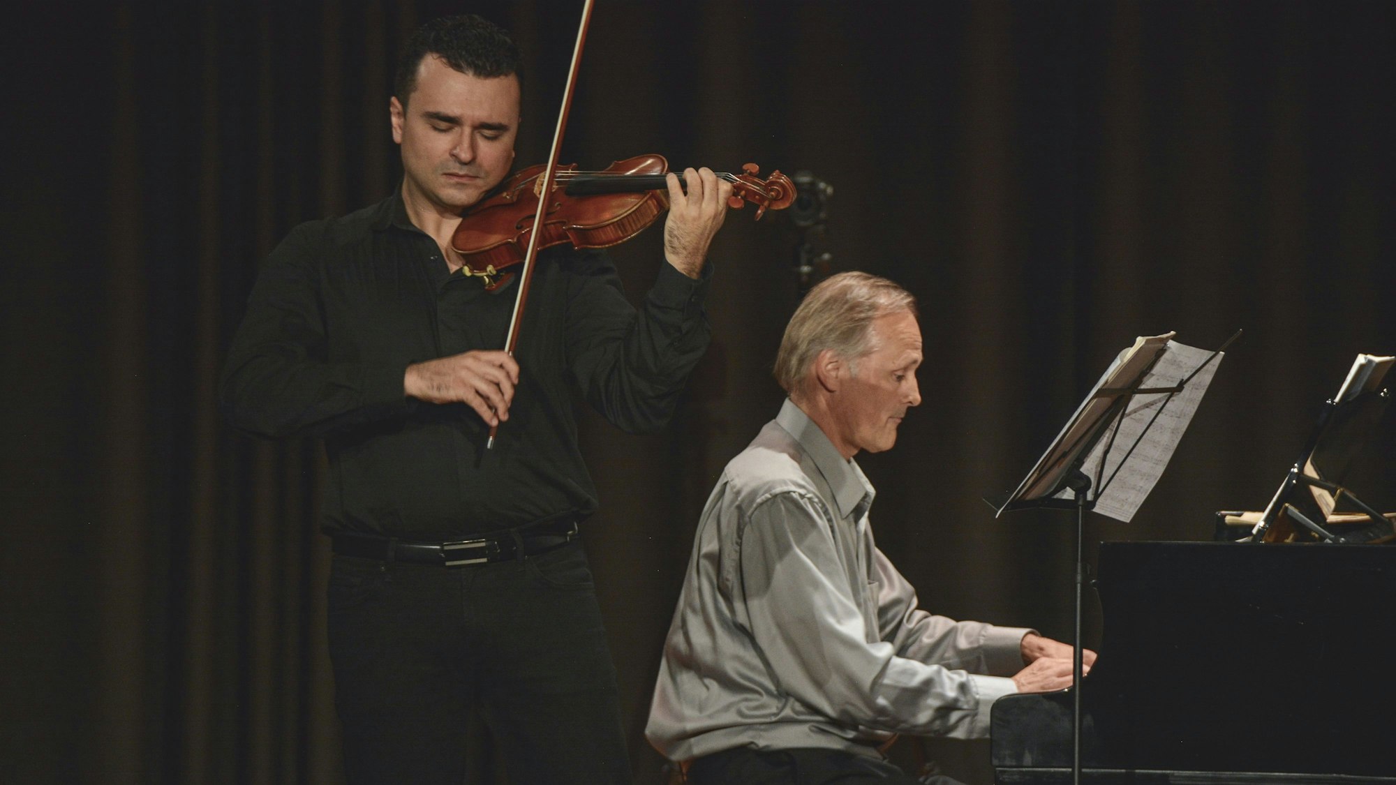 Zwei Musiker auf der Bühne – einer am Klavier und der andere mit Geige.