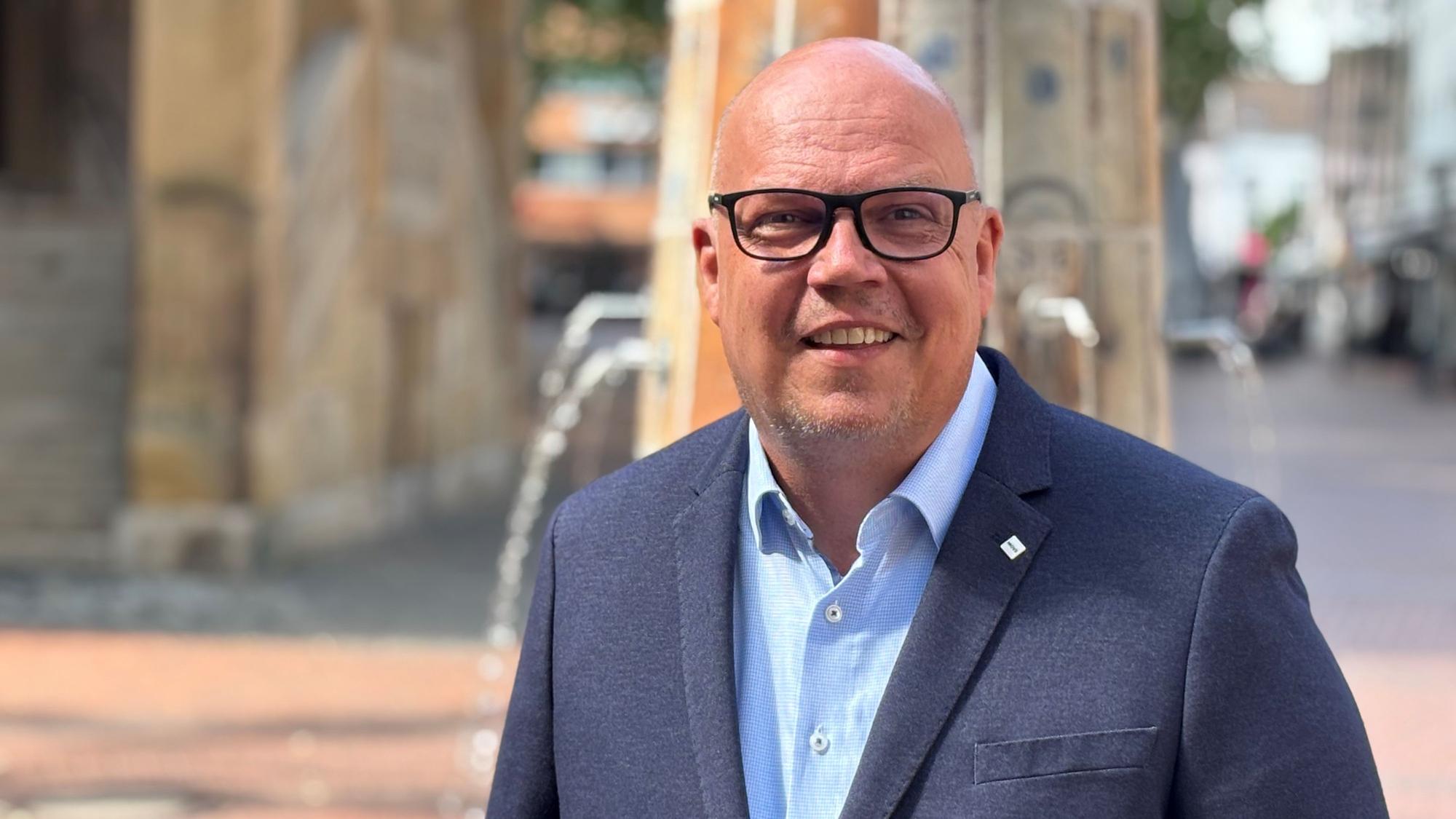 Auf dem Bild ist der Bürgermeisterkandidat der SPD Frechen, Uwe Tietz, zu sehen. Er trägt ein hellblaues Hemd und ein dunkelblaues Sakko.