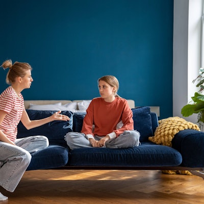 Aufgeregte Mutter, die sich mit ihrem auf dem Sofa sitzenden Kind streitet.