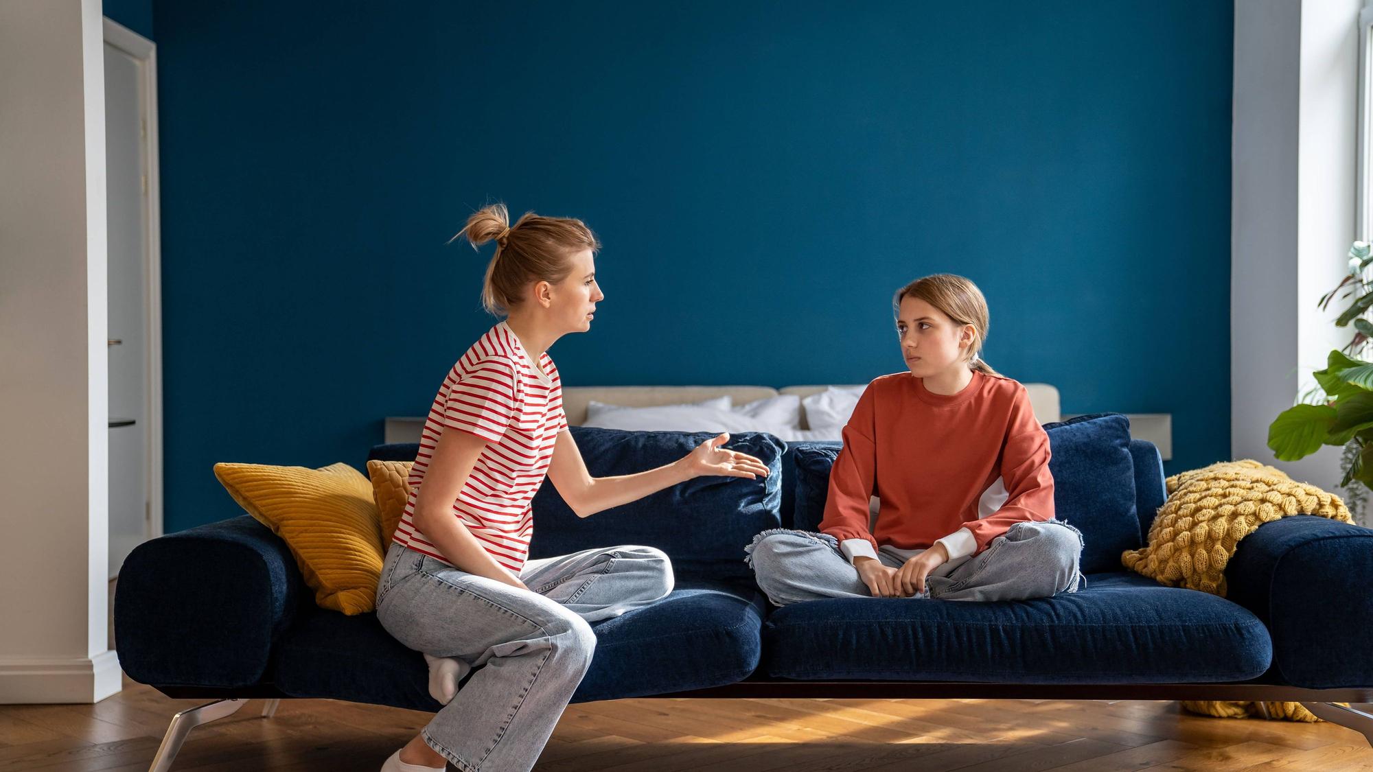 Aufgeregte Mutter, die sich mit ihrem auf dem Sofa sitzenden Kind streitet.