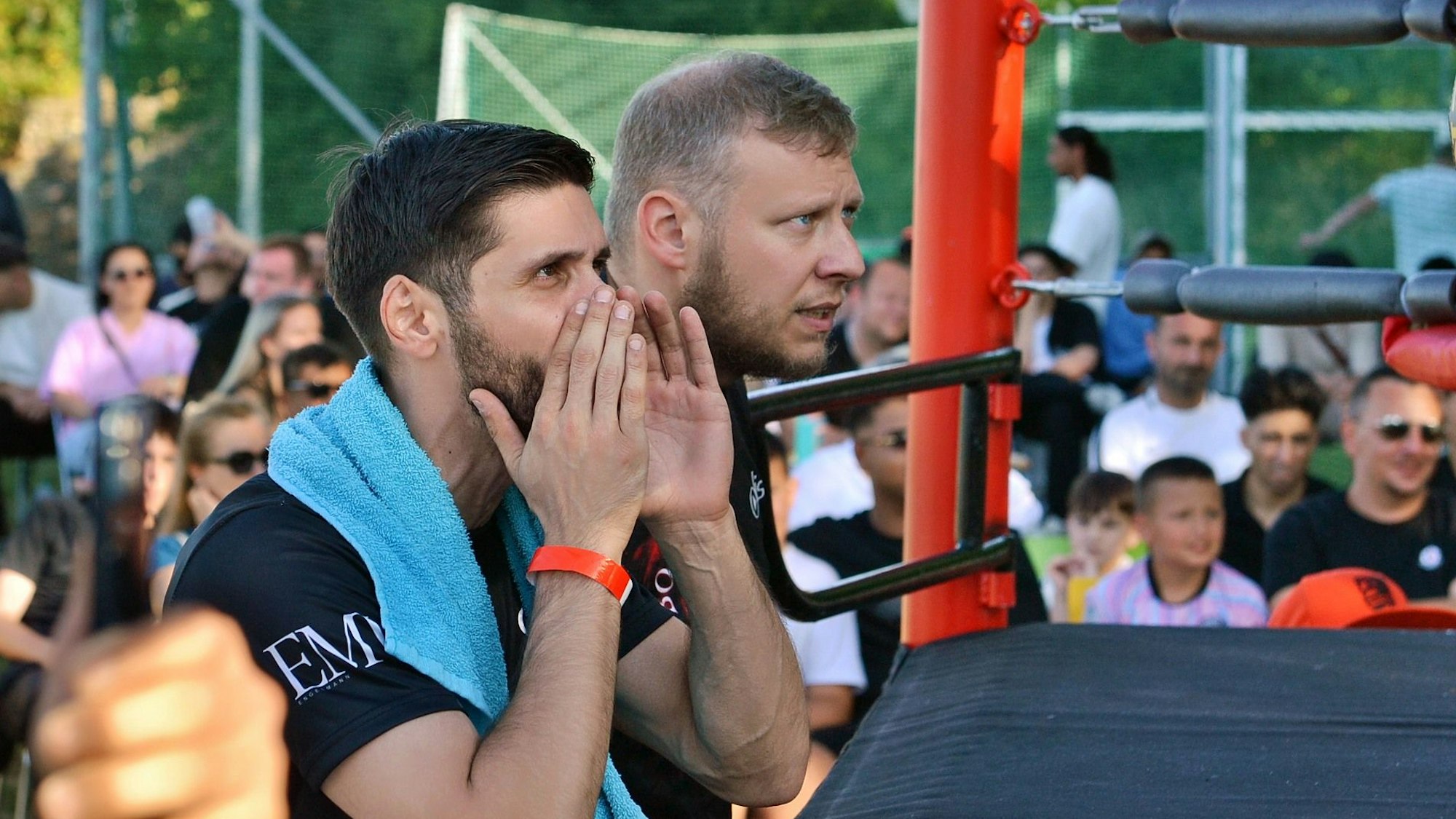 Zwei Trainer stehen an einem Boxring und rufen.