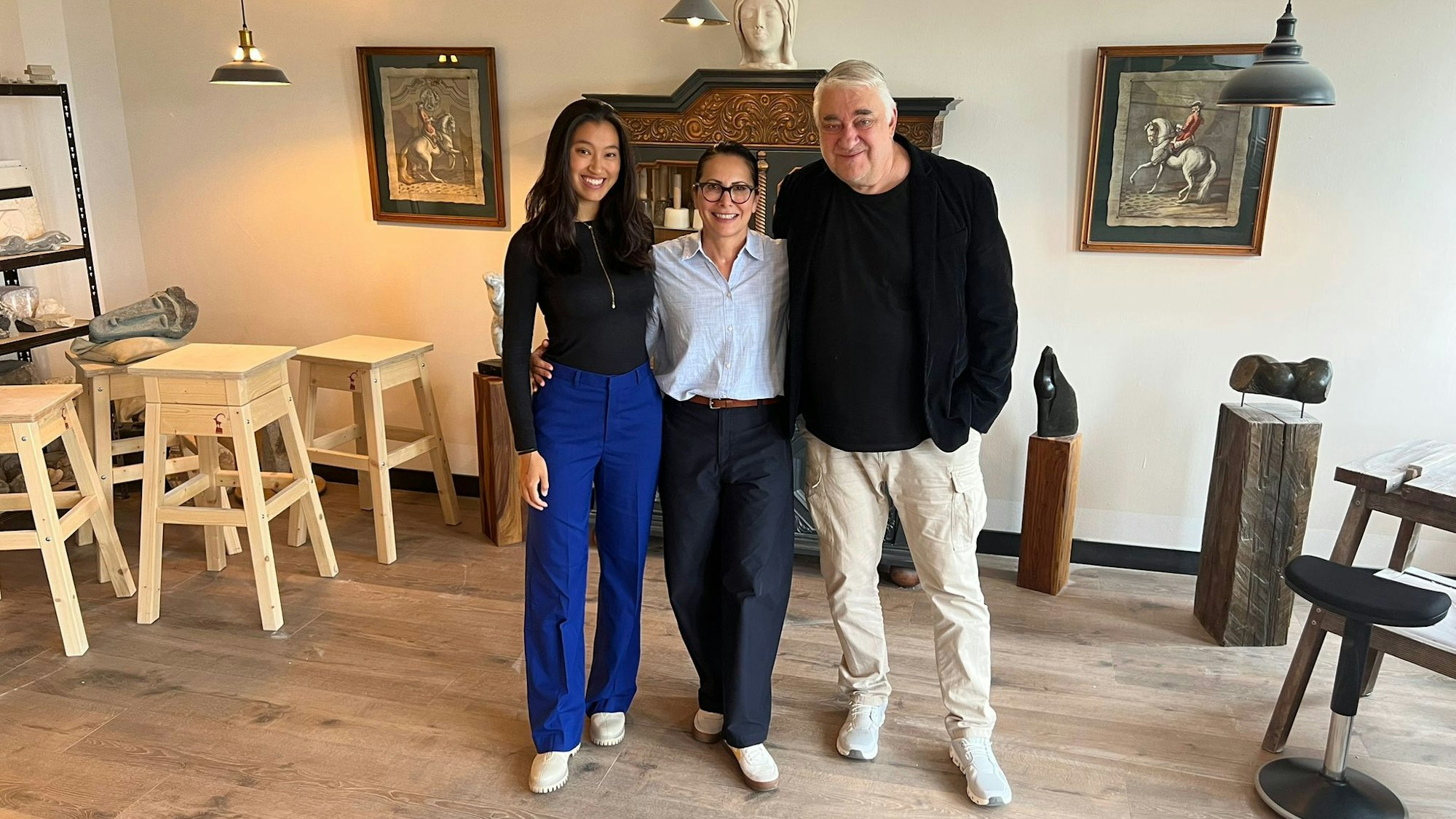 Zwei Frauen und ein Mann stehen in einem Kunst-Atelier.