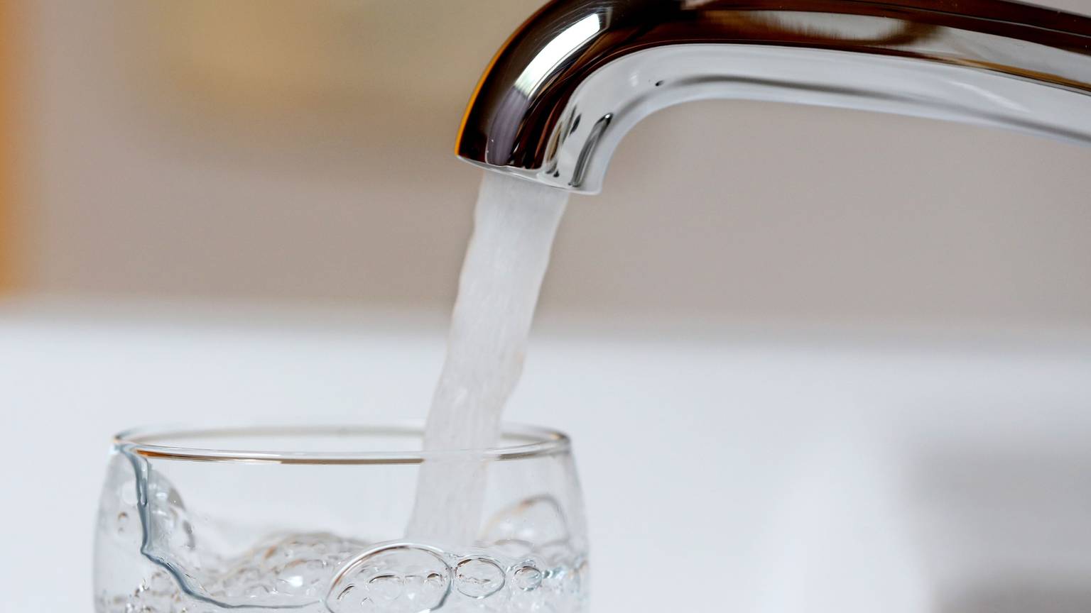 Wasser läuft aus einem Wasserhahn in ein Wasserglas.