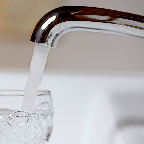 Wasser läuft aus einem Wasserhahn in ein Wasserglas.