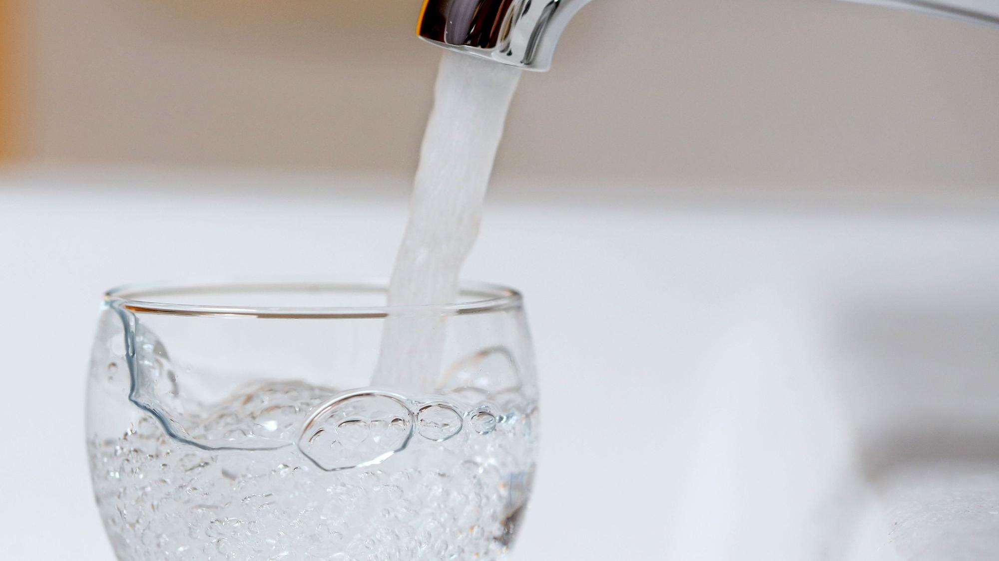 Wasser läuft aus einem Wasserhahn in ein Wasserglas.