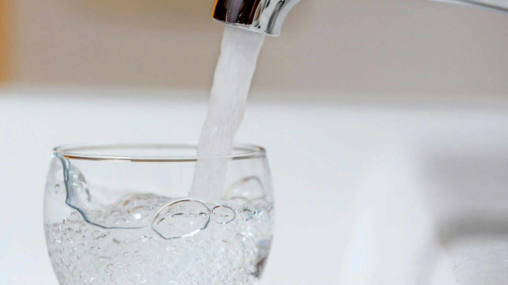 Wasser läuft aus einem Wasserhahn in ein Wasserglas.