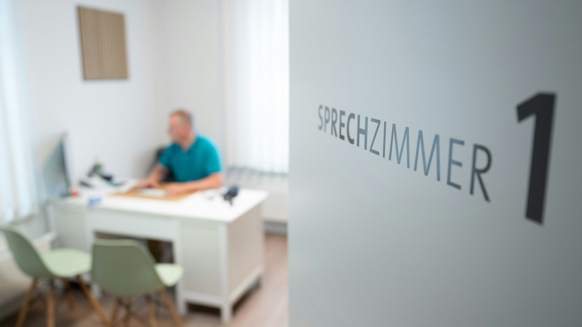Ein Hausarzt sitzt in einem Sprechzimmer seiner Hausarztpraxis an einem Schreibtisch.