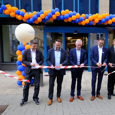 Wiedereröffnung der VR-Bank in Schleiden: Sieben Männer in Anzügen zerschneiden symbolisch ein rot-weißes Flatterband.
