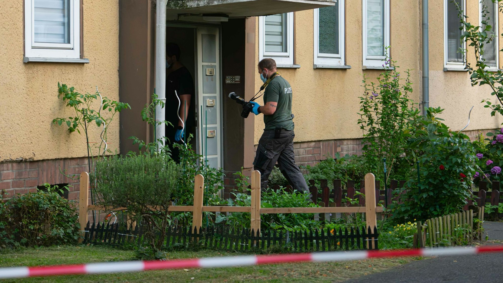 Beamte der Polizei stehen mit Gummihandschuhen vor einer Häuserreihe.