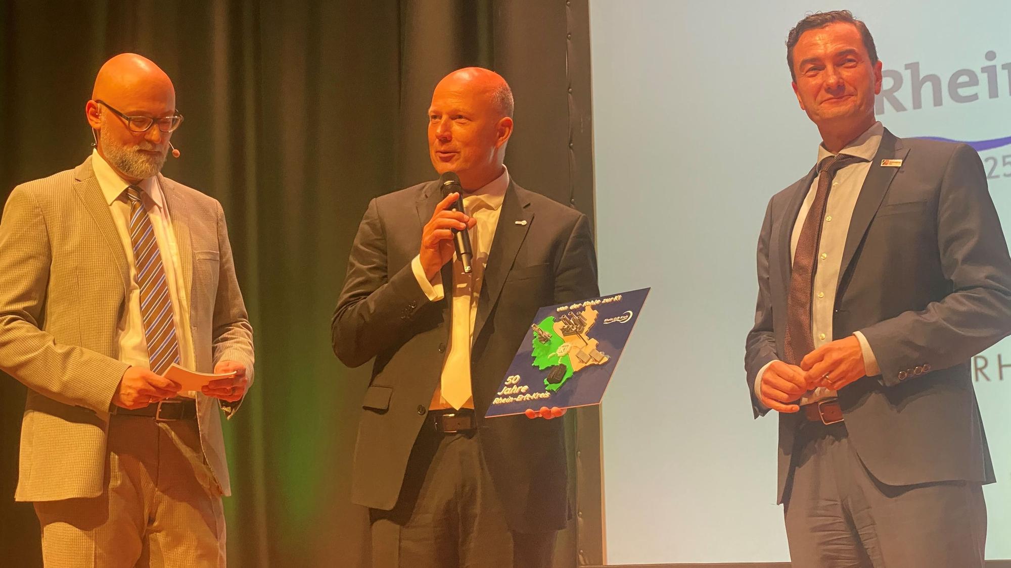 Zu sehen sind Moderator Olly Hahn sowie Frank Rock und Dr. Thomas Wilk auf der Bühne.