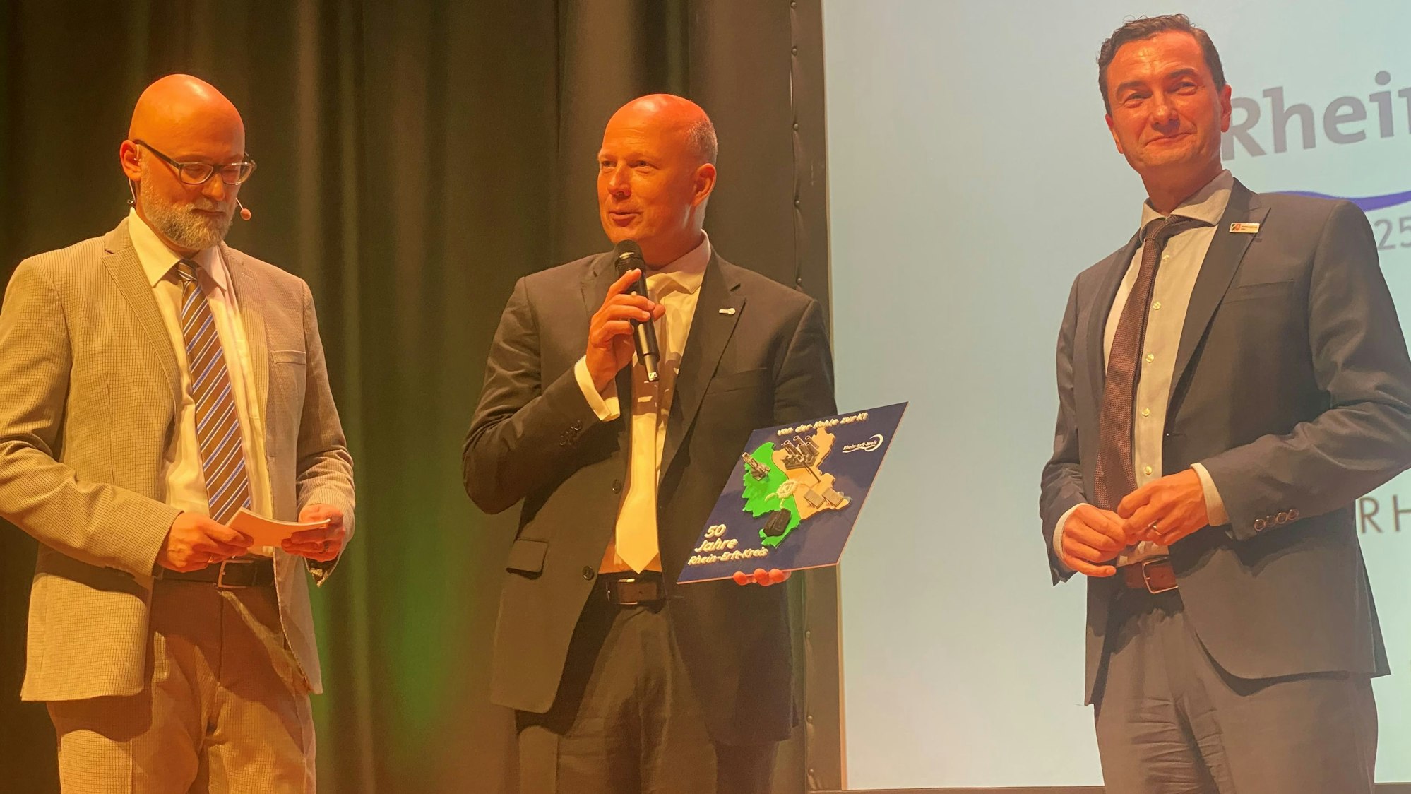 Zu sehen sind Moderator Olly Hahn sowie Frank Rock und Dr. Thomas Wilk auf der Bühne.