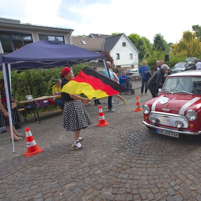 Eine Frau mit Flagge gibt das Startsignal für einen alten Minicooper.