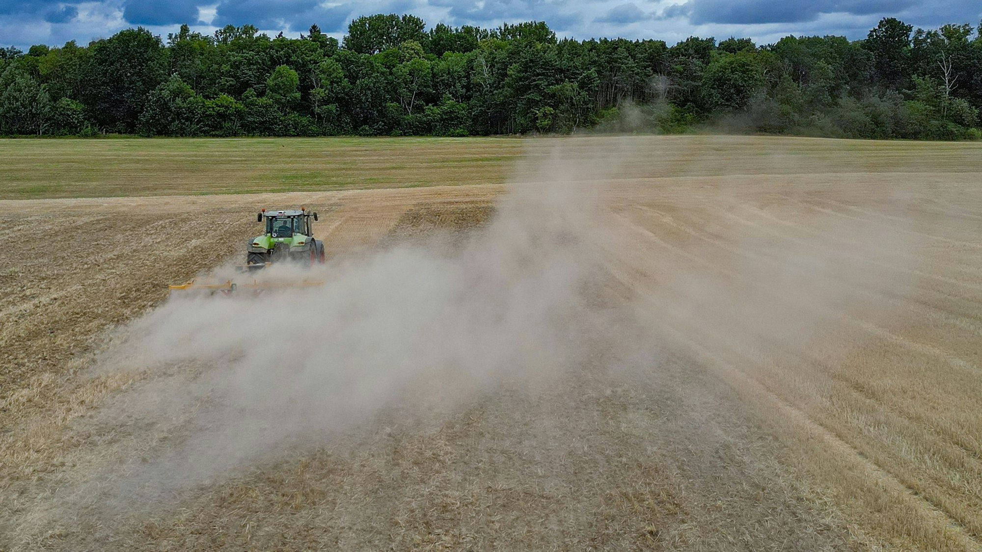 Ein Landwirt fährt mit einer Scheibenegge über ein abgeerntetes Getreidefeld, der trockene Boden staubt. Nennenswerter Regen ist nicht zu erwarten.