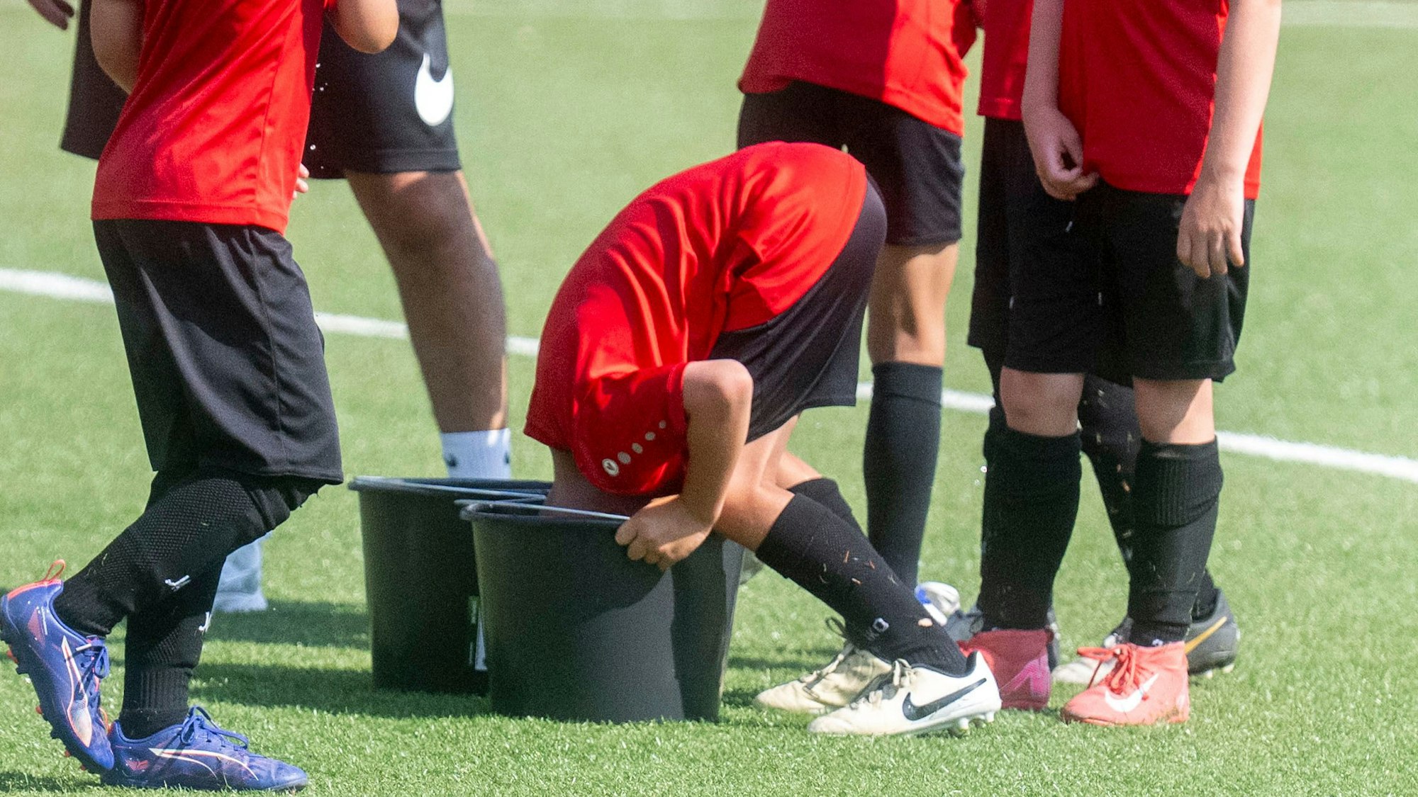 Ein Fußballer steckt seinen Kopf in einen mit Wasser gefüllten Eimer, um sich abzukühlen.