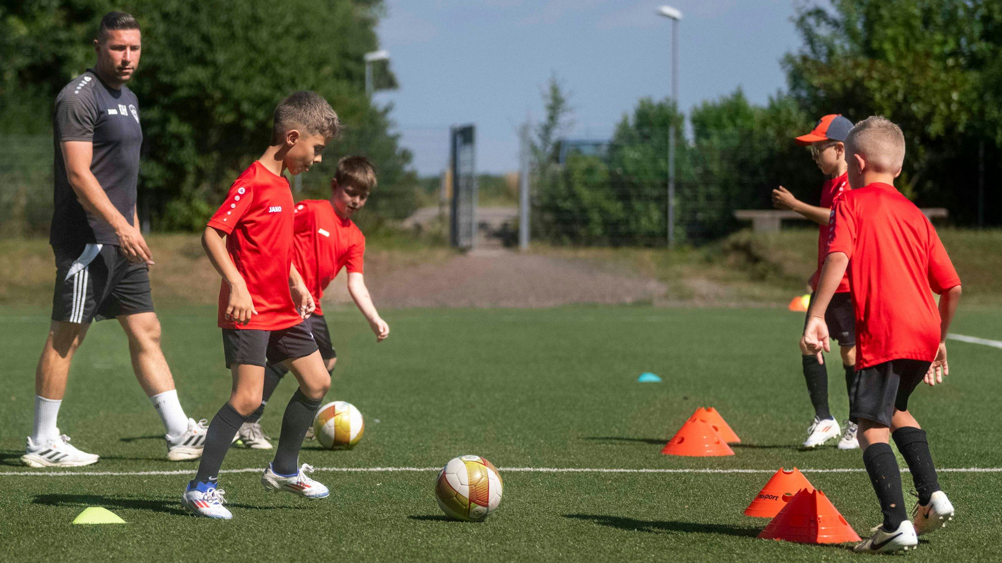 Junge Fußballspieler passen sich Bälle durch Hütchen hindurch zu. Der Trainer beobachtet die Fußballer.