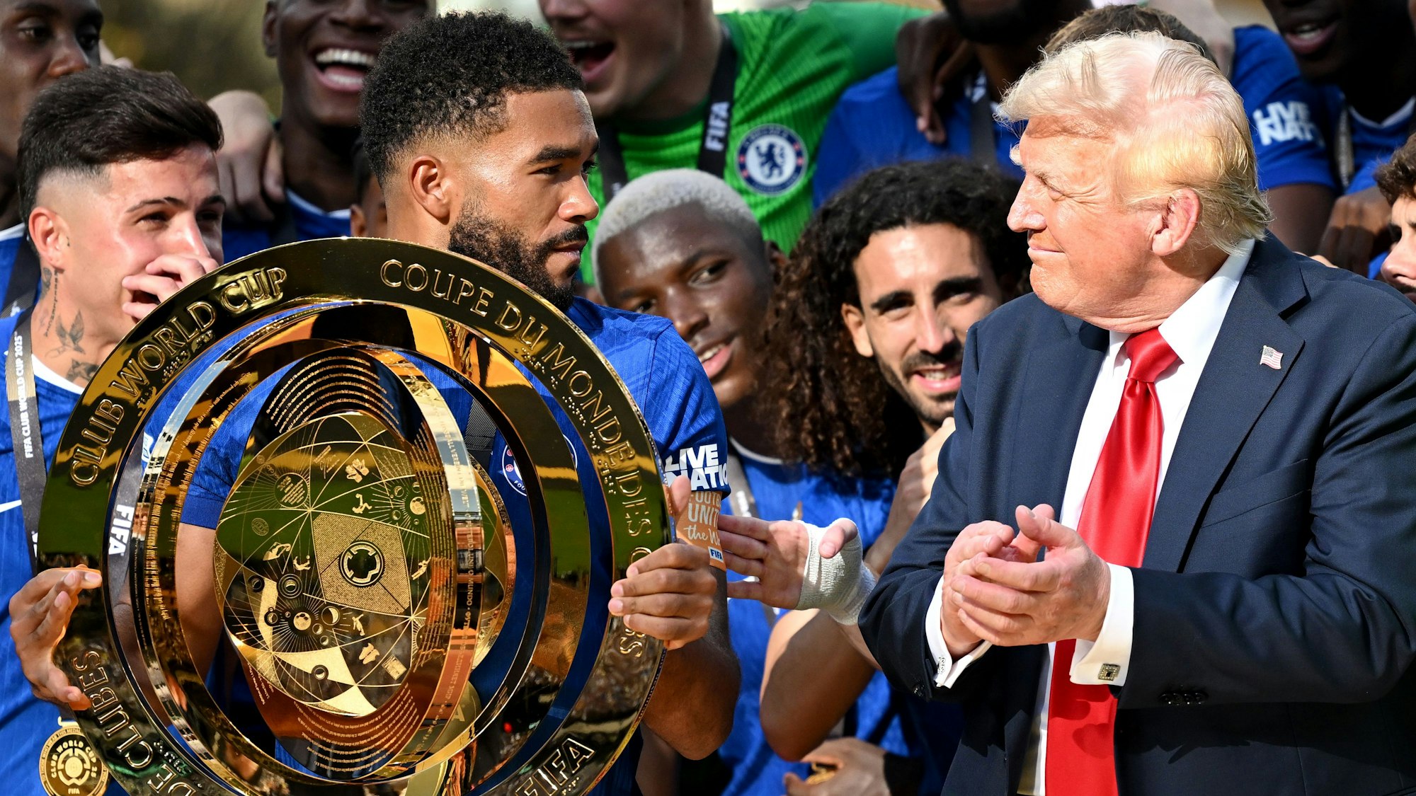 Chelseas Reece James (l/vorn) hält die Trophäe in der Hand und schaut zu US-Präsident Donald Trump.