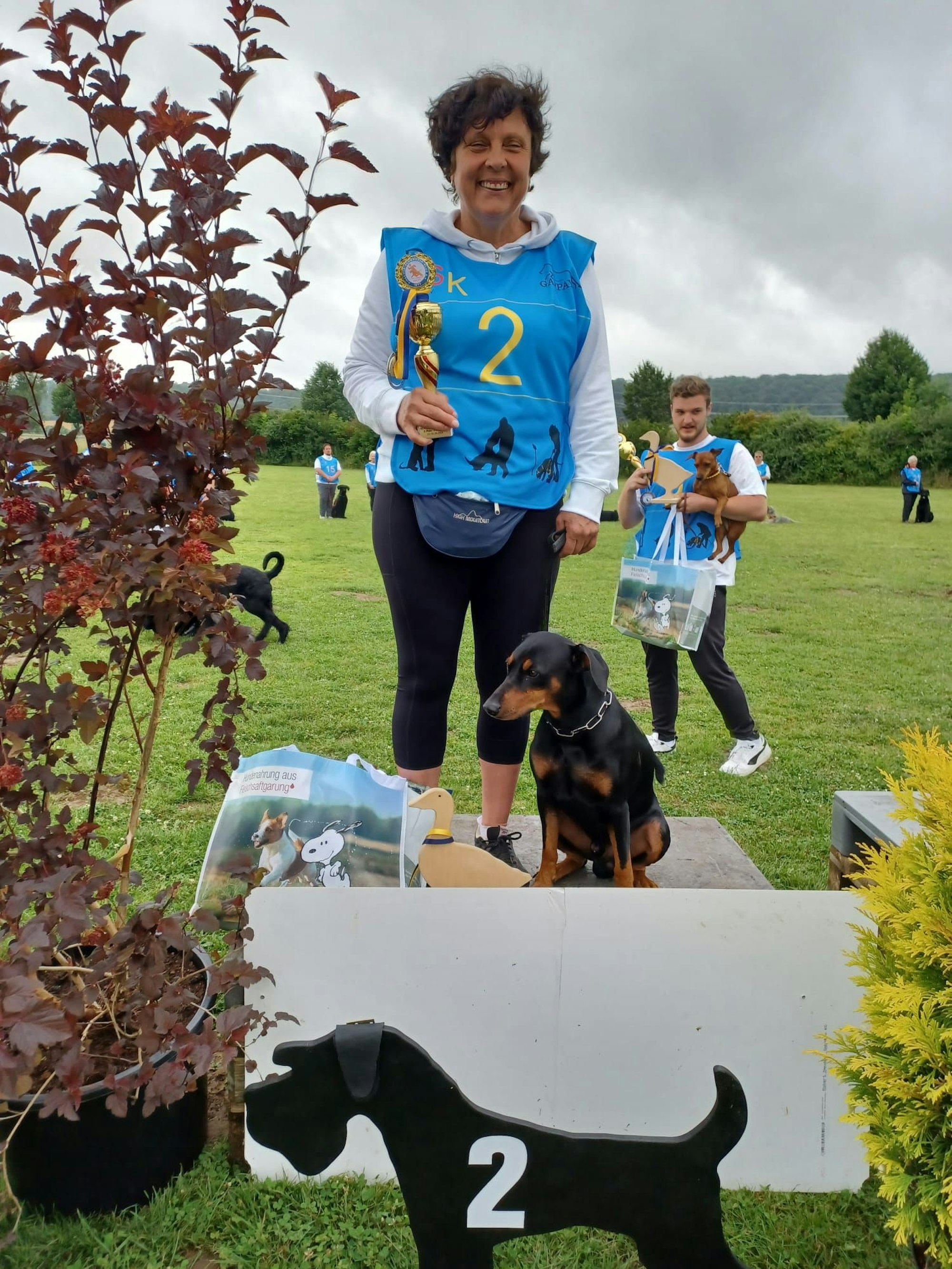 Eine Frau und ihr Hund beim Turnier-Hundesport als Vize-Meister auf dem Podium.