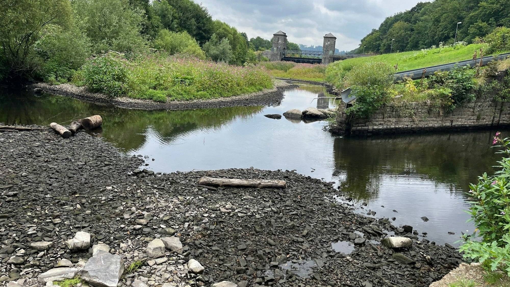 Eine trockene Kiesbank, im Hintergrund eine Wehranlage.