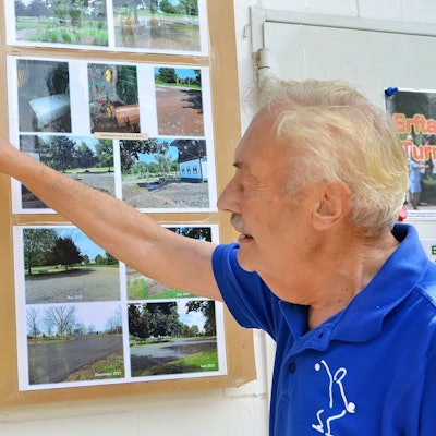 Wolfgang Vieweg zeigt auf Aufnahmen der Flutkatastrophe 2021, die an einer Wand hängen.