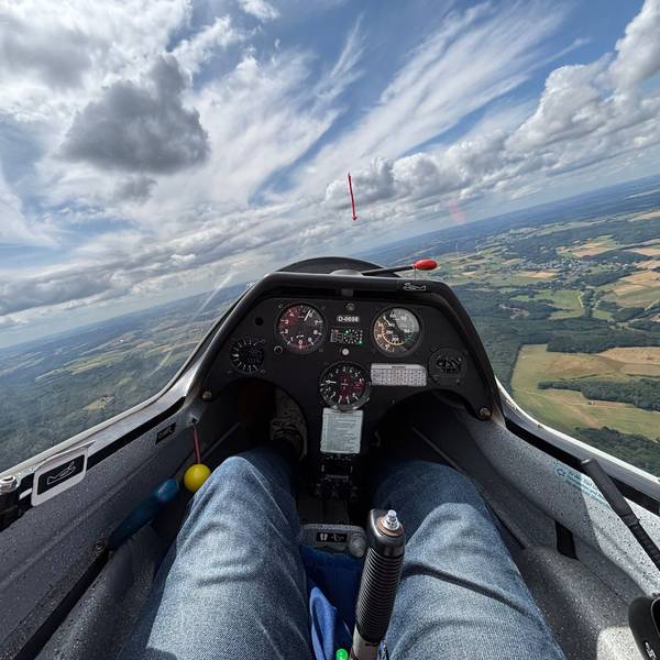 Foto aus einem Segelflugzeug. Der Blick geht aufs Instrumentenbrett, auf die Landschaft unten und die Wolken.