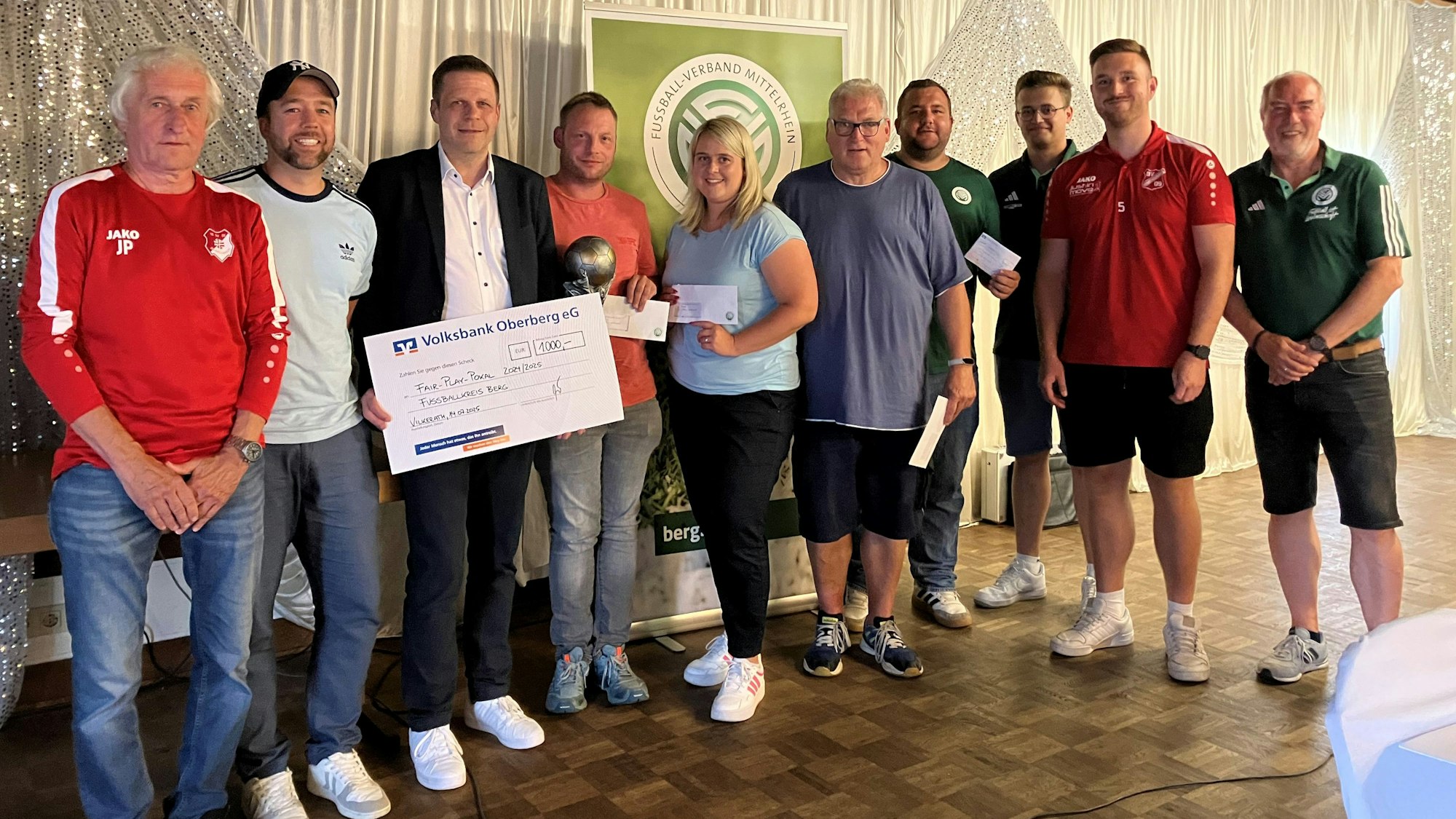 Ein Gruppenfoto verschiedener Vertreter von Fußballvereinen und einem Mitarbeiter der Volksbank, der einen Scheck in der Hand hält.