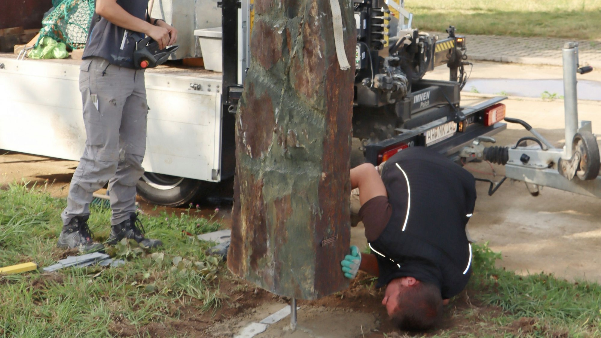 Ein Mann liegt auf dem Boden und hilft dabei, eine Stele an die richtige Stelle in ein Fundament zu setzen.