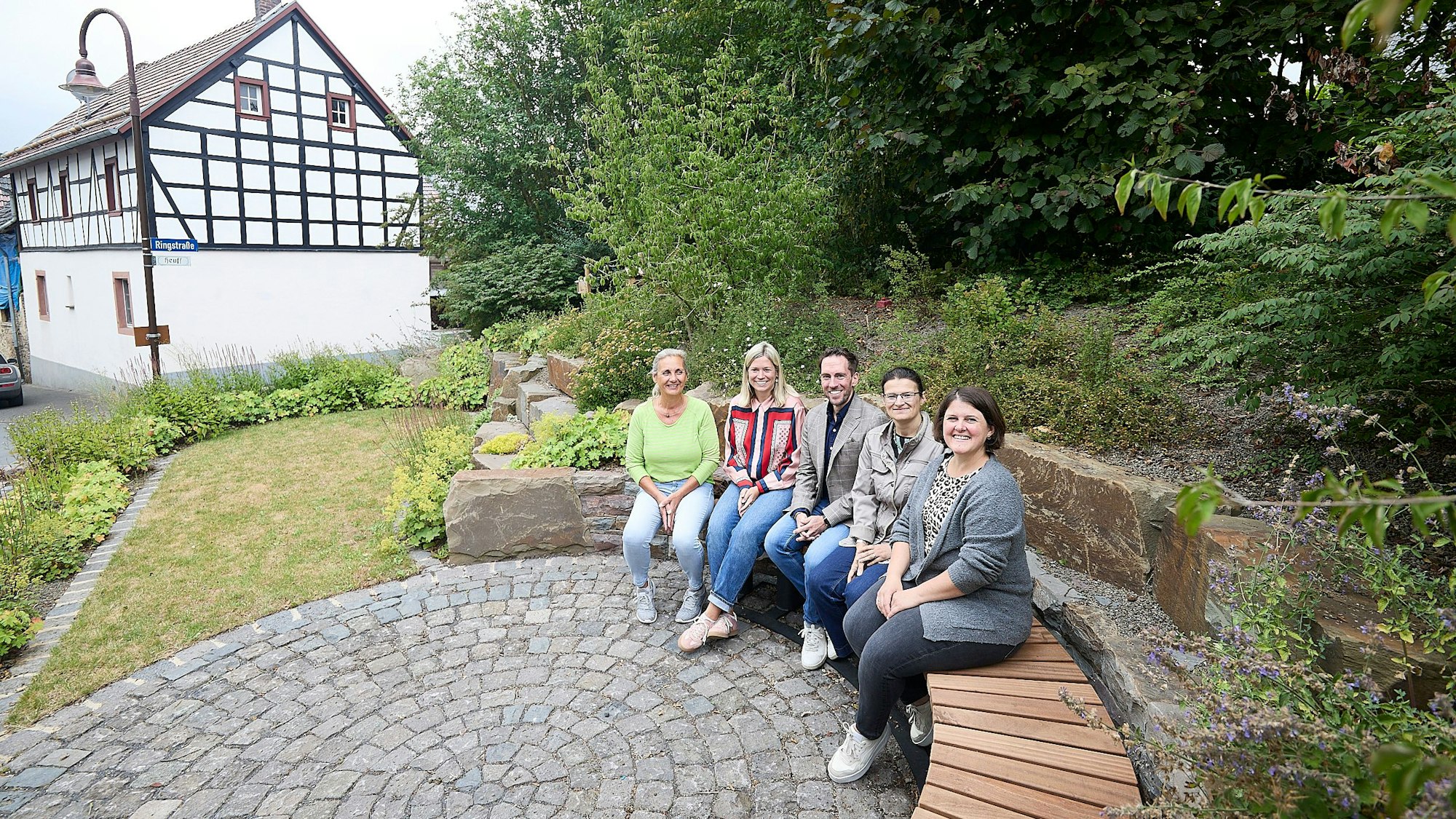 Vier Frauen und ein Mann sitzen auf einer halbrunden Bank auf dem Dorfplatz in Blankenheim-Lommersdorf.