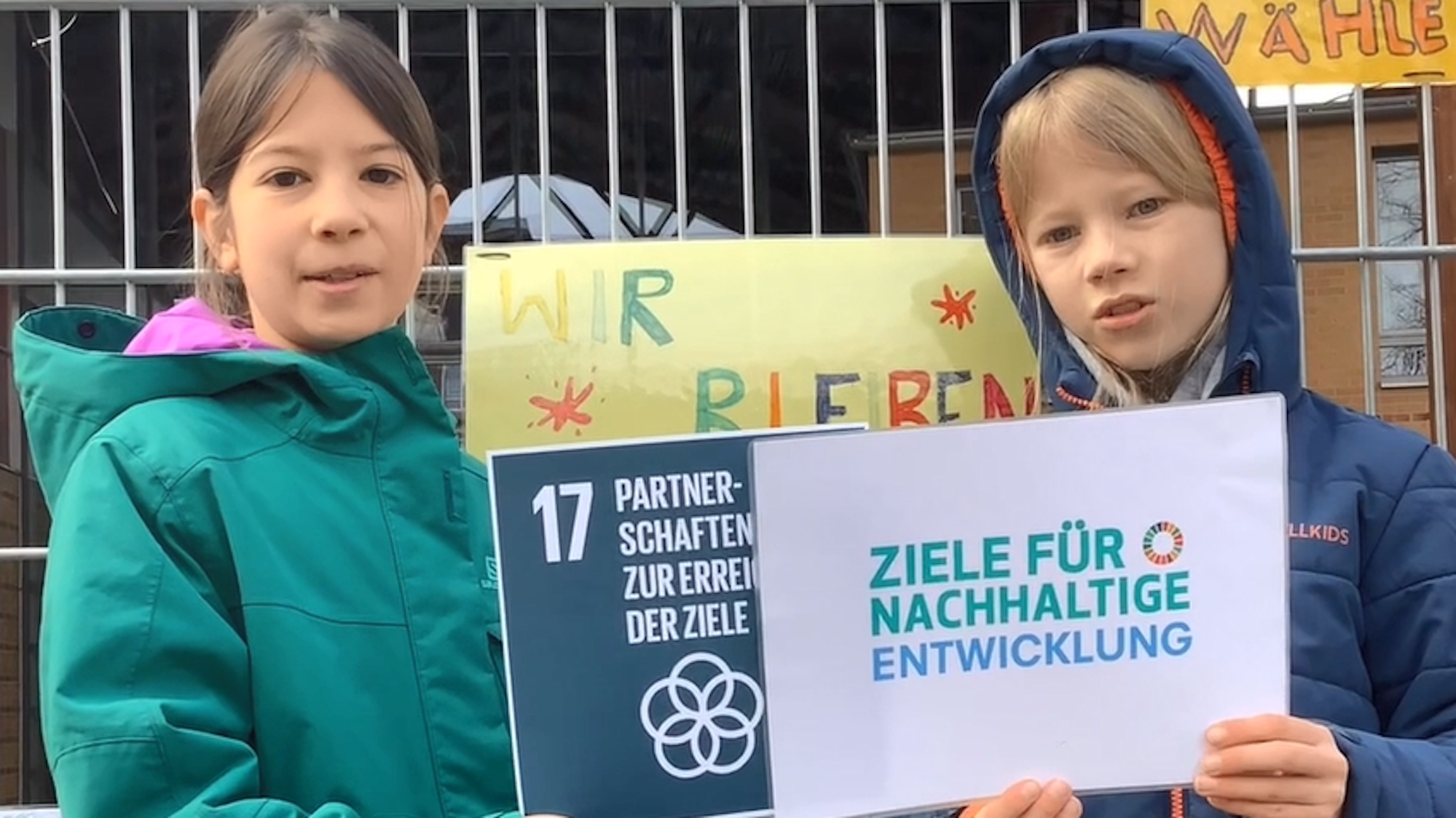Eine Grundschülerin und ein Grundschüler halten ein Schild mit der Aufschrift „Ziele für nachhaltige Entwicklung“.