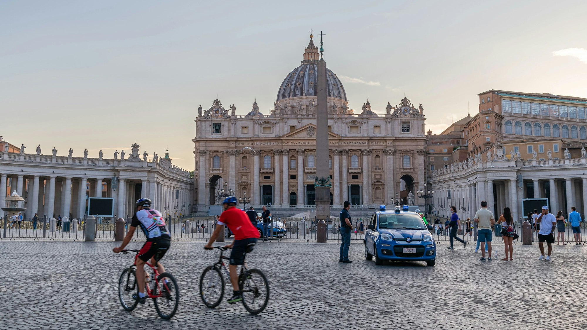 Panoramic early morning scene at St Peter's square with police car and cicylists in foreground in Rome , Italy
