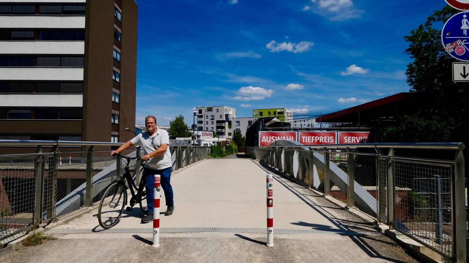 Ein Mann schiebt sein Fahrrad über eine Brücke, die mit zwei Pollern abgesperrt ist für motorisierten Verkehr.