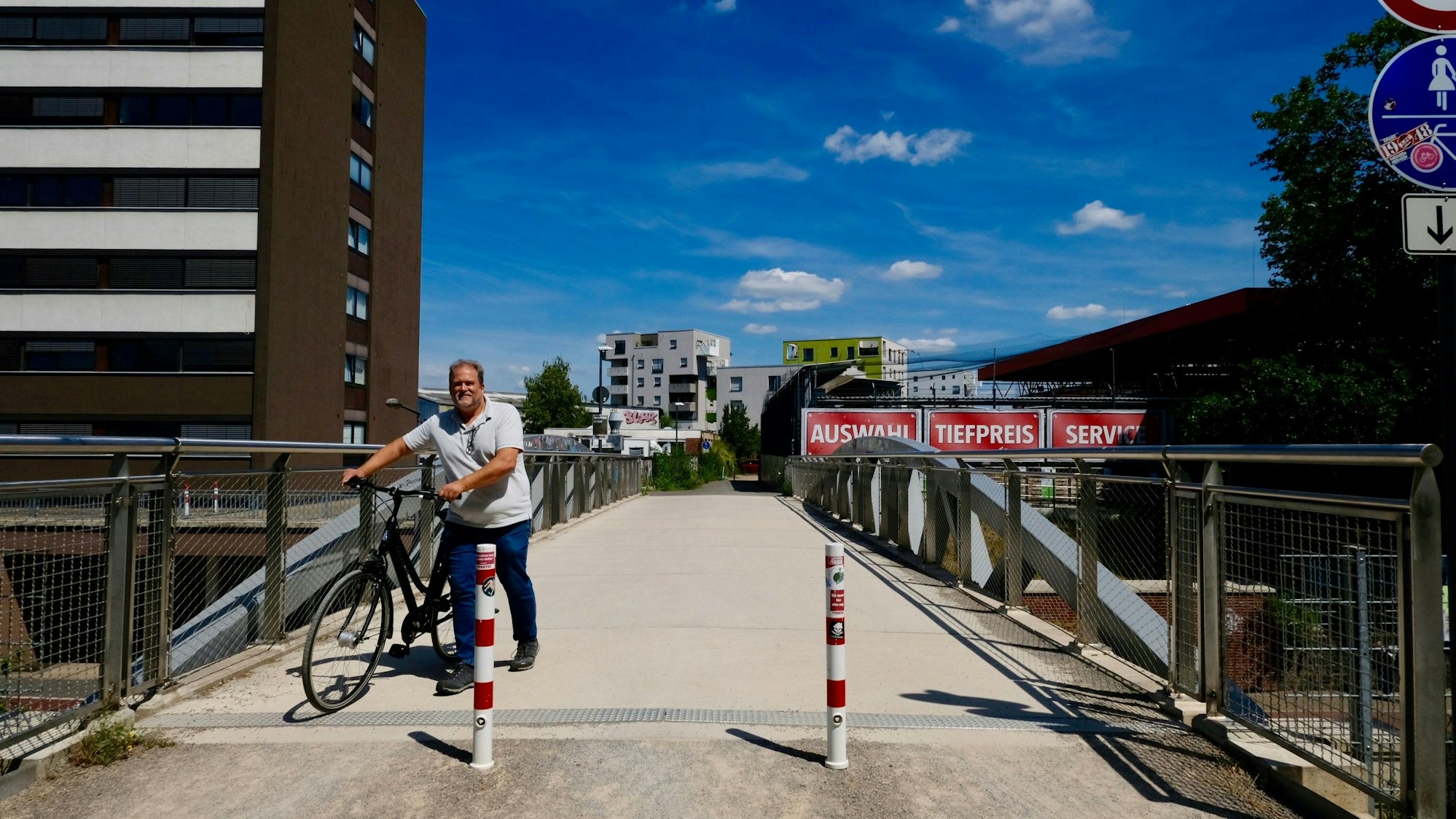 Ein Mann schiebt sein Fahrrad über eine Brücke, die mit zwei Pollern abgesperrt ist für motorisierten Verkehr.