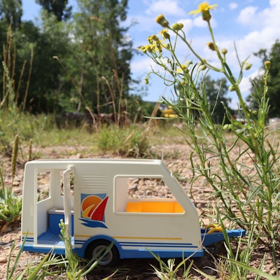 Ein kleiner Spielzeug-Wohnwagen steht auf einem leeren Feld zwischen ein paar Pflanzen in Bad Münstereifel.